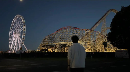 A man looking at a rollercoaster park at night 