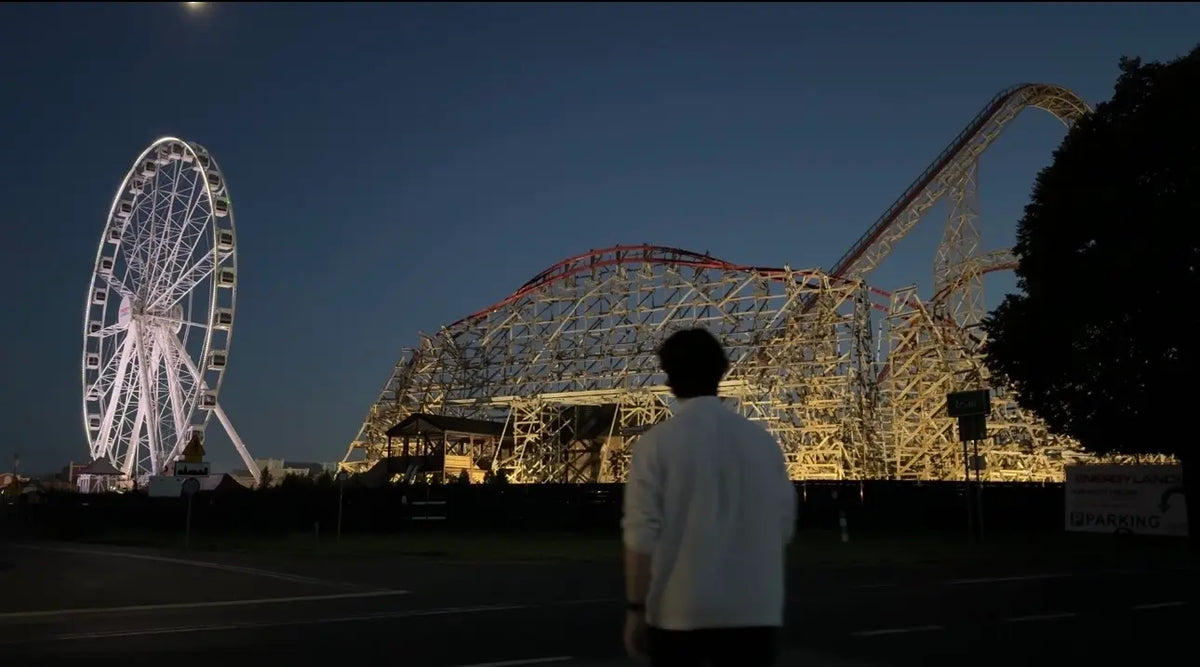 A man looking at a rollercoaster park at night 
