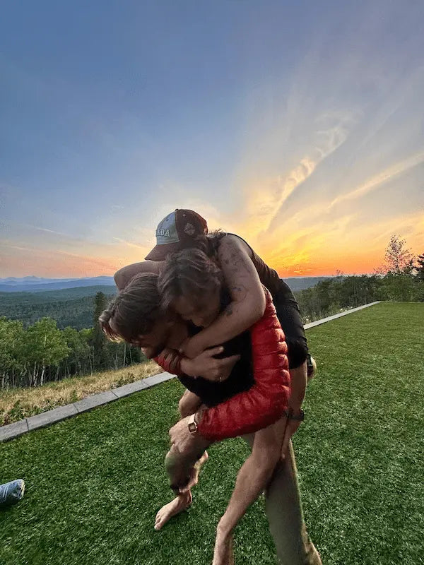 Three friends playfully wrestling at sunset during an outdoor adventure
