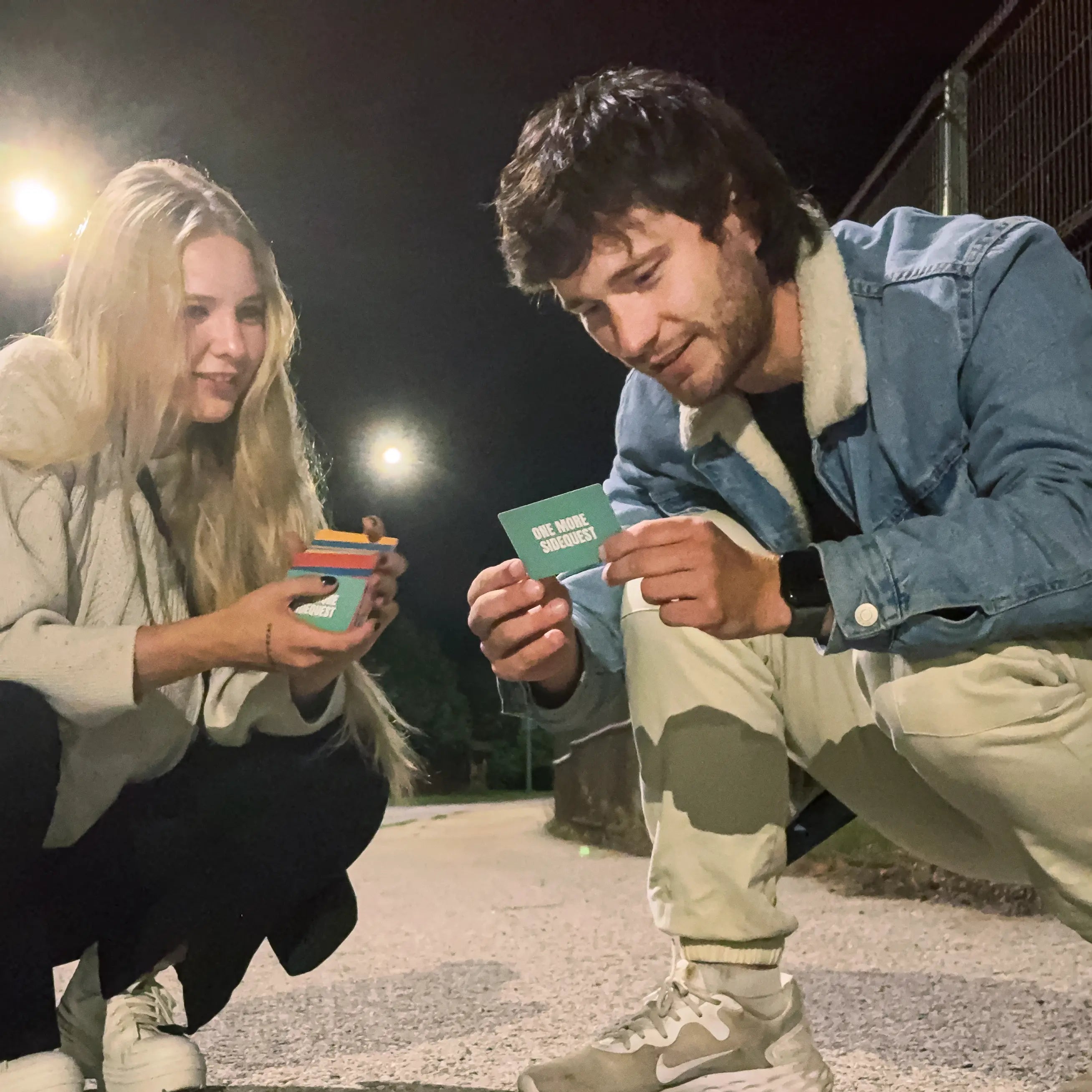 Two people squatting outdoors at night, holding cards with text.