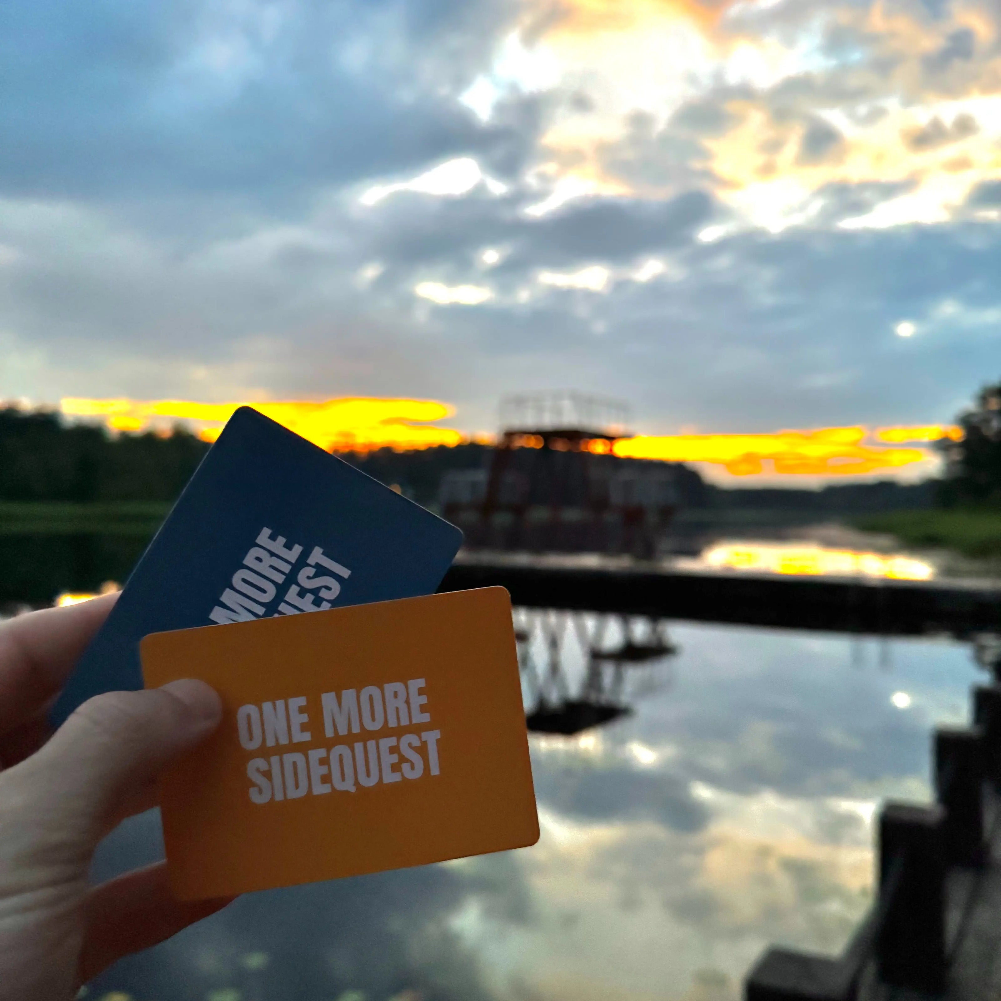 Two cards, one blue and one orange, held in front of a scenic sunset over water.