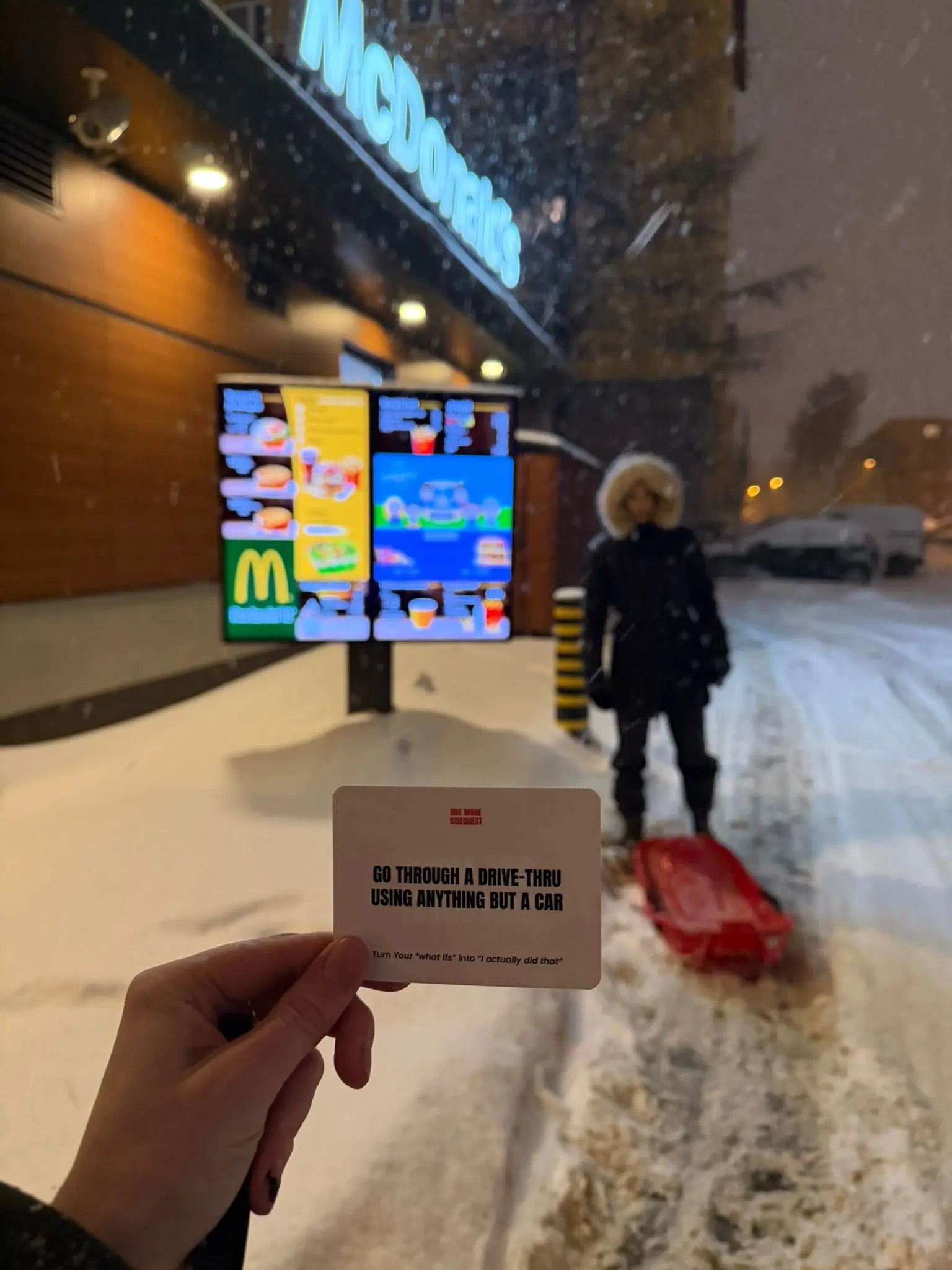 Person holding a card in front of a McDonald's drive-thru with a snowy background